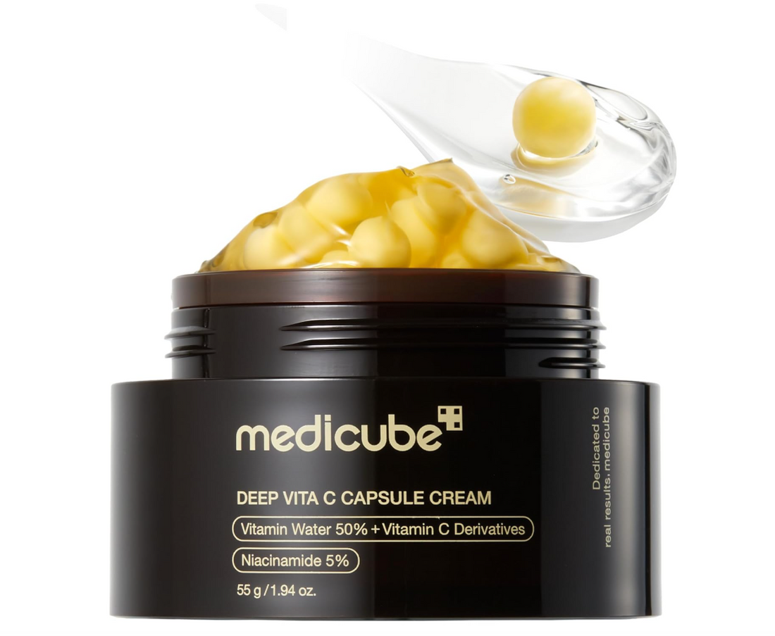 Medicube Deep Vita C Capsule Cream in a black jar with a brown lid, shown open with yellow capsules visible and a clear spoon lifting some cream, on a white background. Medicube Deep Vita C Capsule Cream 55g