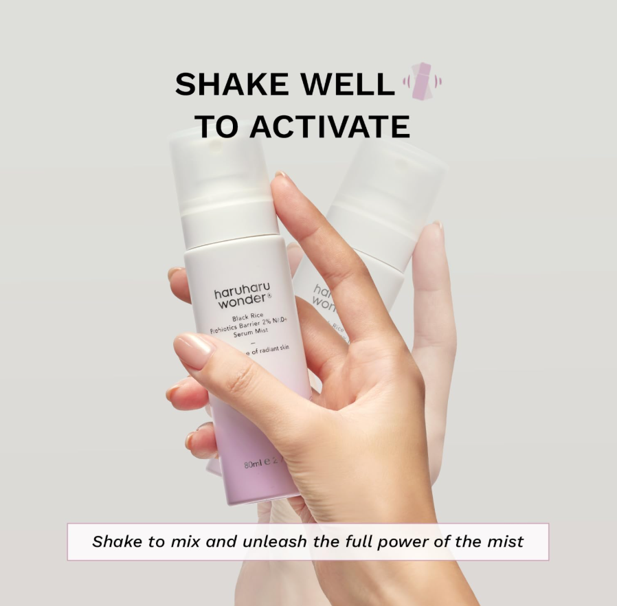 Hand holding a white and purple skincare mist bottle with text on a light gray background, Haruharu Wonder Black Rice Probiotics Barrier 2% NAD+ Serum Mist 80ml