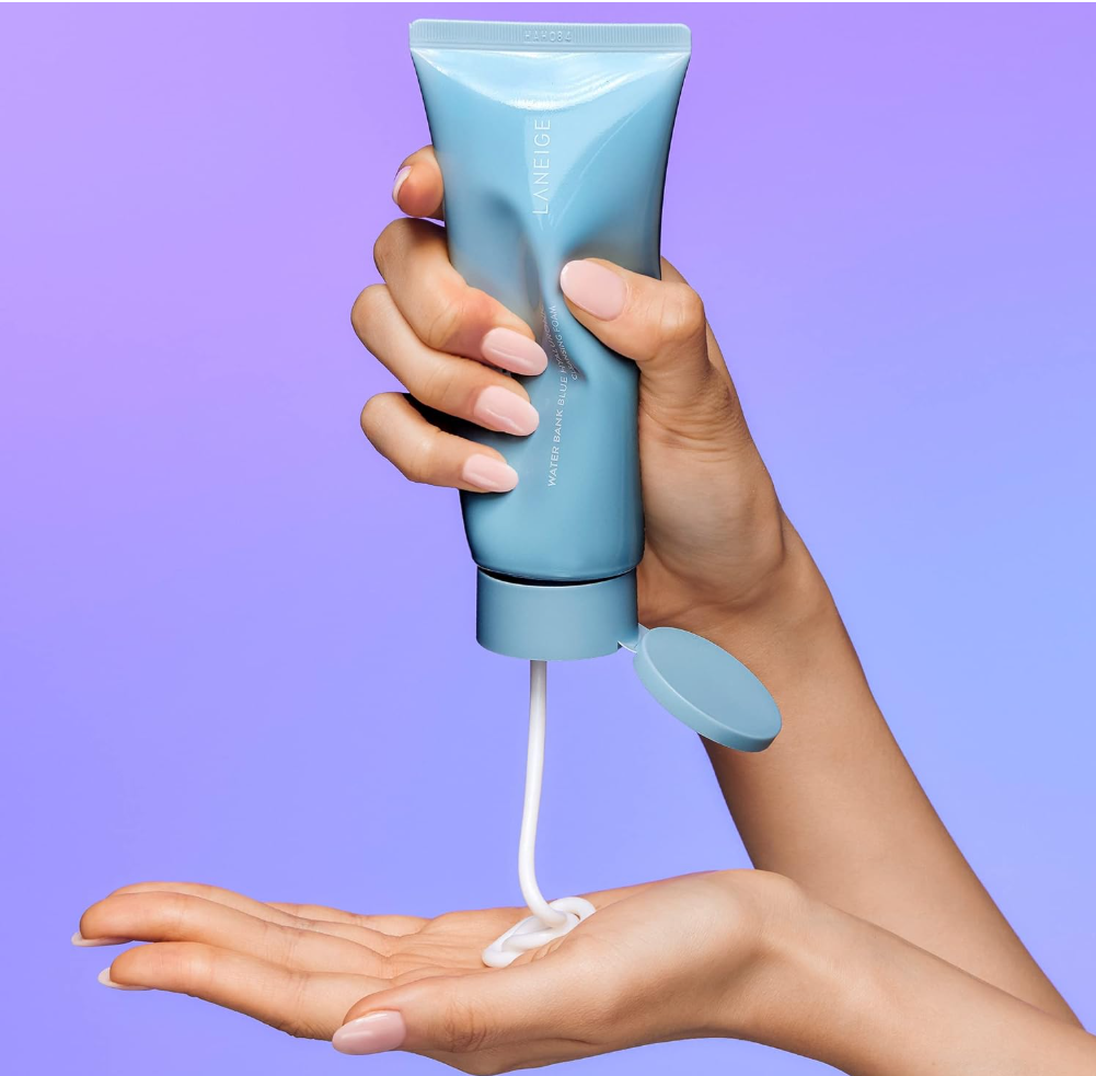 Hand holding a blue tube of cream with white cream being dispensed onto another hand against a purple background, Langie Water Bank Blue Hyaluronic Cleansing Foam 150g