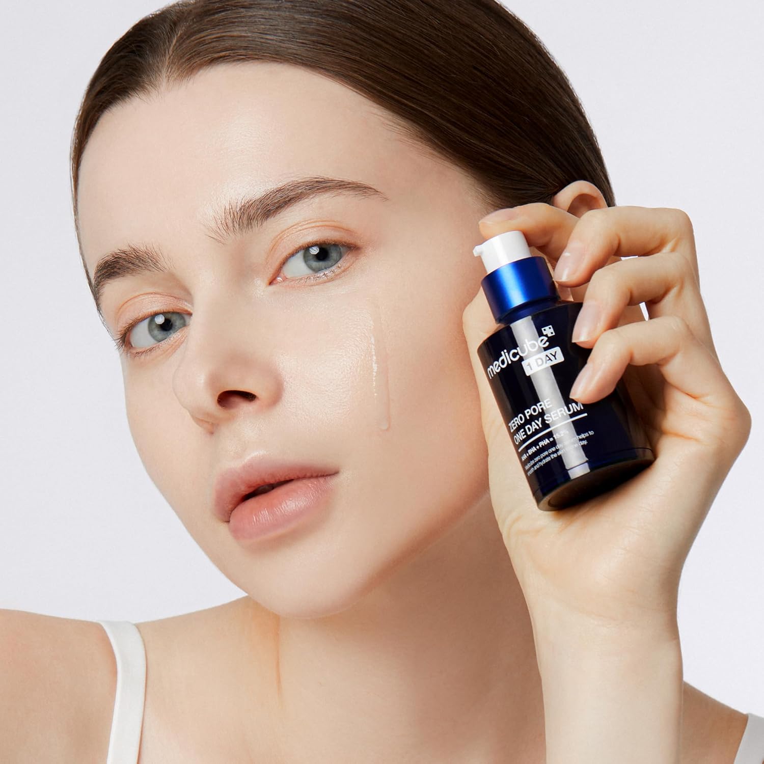 Woman holding a skincare serum bottle close to her face on a plain background, Medicube Zero Pore One Day Serum 30ml