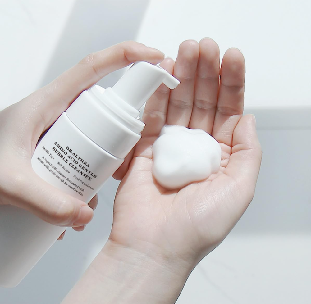 Hand holding a white bottle of bubble cleanser with foam on a light background, Dr.Althea Amino Acid Gentle Bubble Cleanser 140ml
